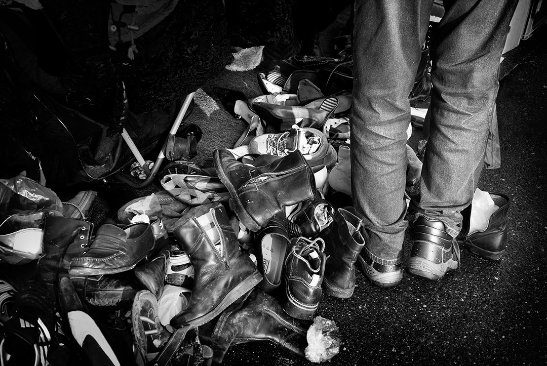 Piled shoes beside a person’s legs.